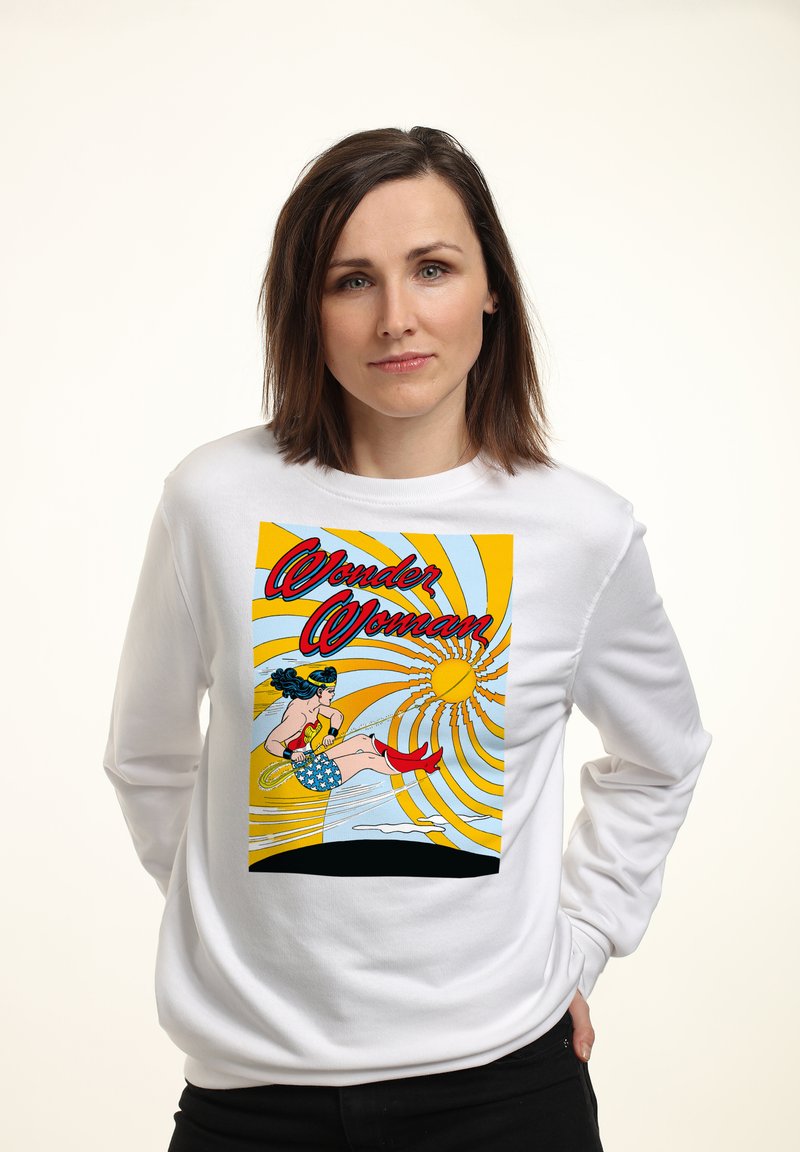 Biały sweter z kolorową grafiką Wonder Woman na tle żółtego promieniowania słońca, z czerwonymi akcentami i niebieskimi elementami w designie.