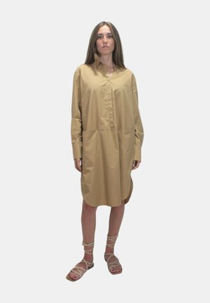 Abito camicia beige con scollatura a colletto e chiusura a bottoni, dotato di maniche lunghe e due tasche frontali, abbinato a sandali con cinturini.