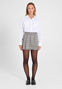 Camicia bianca a maniche lunghe con due tasche sul petto, abbinata a una gonna mini in tartan grigia. Collant neri e mocassini con dettagli dorati completano il look.