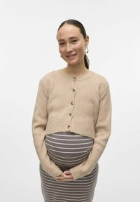 Svetlo bež rebrast kardigan z okroglim izrezom in šestimi gumbi, v kombinaciji z rjavim in belim prugastim oblekom.