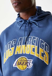 Sweat à capuche bleu avec les inscriptions "LOS ANGELES" et "LAKERS" brodées en jaune et blanc, doté d'une capuche à cordon de serrage et d'un tissu texturé.