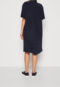 Robe bleu marine à manches courtes avec une coupe décontractée, dotée d'une fente dans le dos et d'une texture lisse. Associée à des baskets bleu marine.