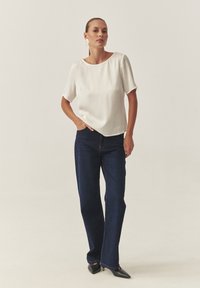 Blusa blanca de manga corta con cuello redondo combinada con jeans de mezclilla azul oscuro de cintura alta y zapatos negros con punta.