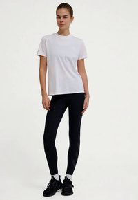 Witte T-shirt met korte mouwen en ronde hals, gecombineerd met zwarte leggings met een subtiel chevronpatroon en witte sportschoenen.