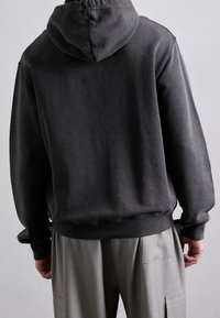 Felpa con cappuccio grigia scura, caratterizzata da una consistenza morbida, vestibilità rilassata e polsini e orlo a costine. Sono visibili anche pantaloni grigi chiari.