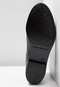 Black rubber shoe sole with diamond pattern; features branding "TOMMY HILFIGER" and size "37" embossed. Smooth finish with textured details.