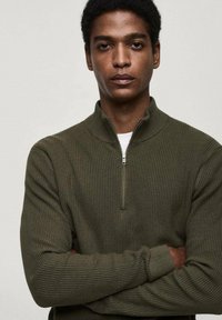 Pulover zip-up de culoare verde măslin, cu o textură canelată și guler înalt, având un fermoar scurt în față și mâneci lungi.