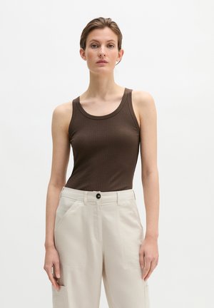 Woman standing wearing a sleeveless brown ribbed top and high-waist beige pants with pockets against a plain white background.