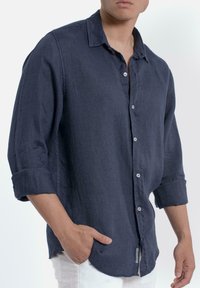 Navyblauw linnen shirt met een button-down kraag, opgerolde mouwen en een relaxte pasvorm. Het heeft witte knopen en een gebogen zoom.