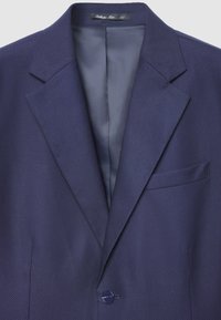 Blazer texturé bleu marine avec revers crantés, fermeture à un bouton et une poche poitrine. Intérieur avec une doublure lisse et contrastante.