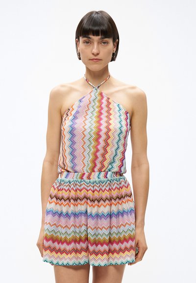Femme portant un haut sans manches à col licou et un short taille haute assorti avec un motif zigzag coloré, debout devant un fond blanc.