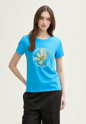 T-shirt bleu vif en coton, avec un graphique floral doré et un texte blanc. Col rond et manches courtes avec une coupe décontractée.