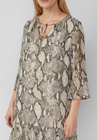 Langärmlige Bluse aus leichtem Stoff mit einem beige-schwarzen Schlangenprint, mit einer gebundenen Halslinie und ausgestellten Ärmeln.