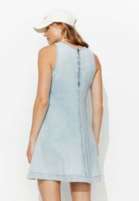 Robe en denim bleu clair au design sans manches, avec une fermeture à boutons au dos et une silhouette évasée, présentant un ourlet brut et une texture subtile.