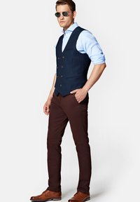 Granatowa, podwójnie zapięta kamizelka, jasno-niebieska koszula, brązowe spodnie slim-fit, brązowe skórzane buty i ciemne okulary przeciwsłoneczne.