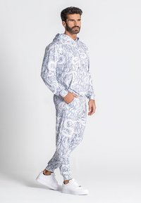 Set di felpa con cappuccio e pantaloni joggers bianchi con un intricato motivo a serpente blu e fiori, dotato di cordoncino e polsini elasticizzati.