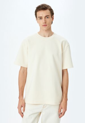 Kremowy, krótko rękawowy t-shirt wykonany z miękkiej bawełny. Posiada okrągły dekolt i luźny krój z minimalną ilością szwów.