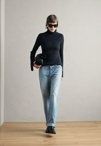 Maglione a collo alto nero a costine, jeans azzurri chiari e stivaletti neri; tiene una borsa nera. Tessuto liscio, top aderente, design dei jeans rilassato.