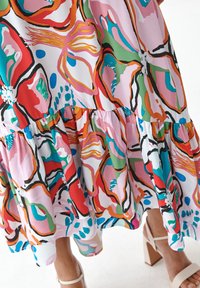 Kapitánka sukně s živým abstraktním květinovým vzorem v růžové, červené, zelené, modré a oranžové, nošena s béžovými sandály na blokovém podpatku.