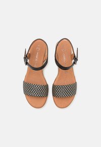 Sandales en cuir noir avec une lanière tressée noire et blanche, dotées d'une boucle à la cheville et d'une semelle intérieure rembourrée marron.