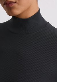 Zwarte geribde coltrui met een getailleerd ontwerp, met een hoge hals en een textuur die verticale lijnen accentueert.