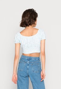 Top cropped azul claro com mangas bufantes e cintura franzida, apresentando um padrão floral. Combinado com jeans azuis de cintura alta.