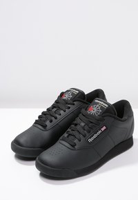 Baskets noires Reebok en cuir, avec une texture lisse, un design à lacets, une boîte à orteils perforée et des accents de logo sur la languette.