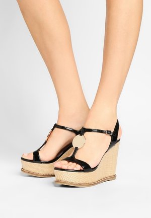 Musta kiiltävän nahkaiset kiilakorokepohjaiset sandaalit, joissa on T-strap-muotoilu, pyöreä koriste ja pohjassa kutojajutamainen rakenne.