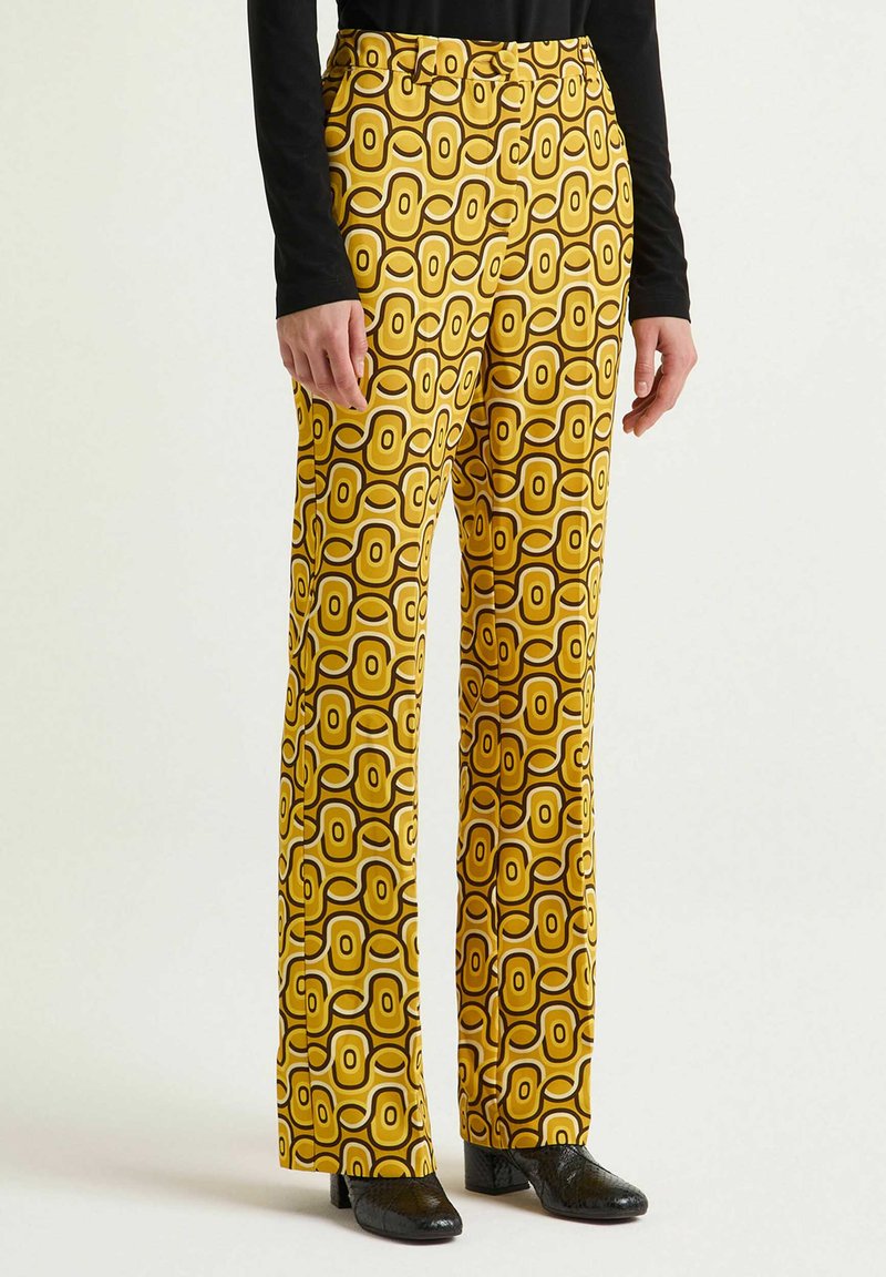 Pantaloni gialli a motivo geometrico con forme circolari e contorni scuri a contrasto. Realizzati in tessuto liscio, taglio a gamba dritta.
