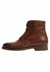 Bota de tobillo de cuero marrón con punta redonda, diseño de cordones y detalles de costura. Tacón plano y ligera textura en la superficie del cuero.