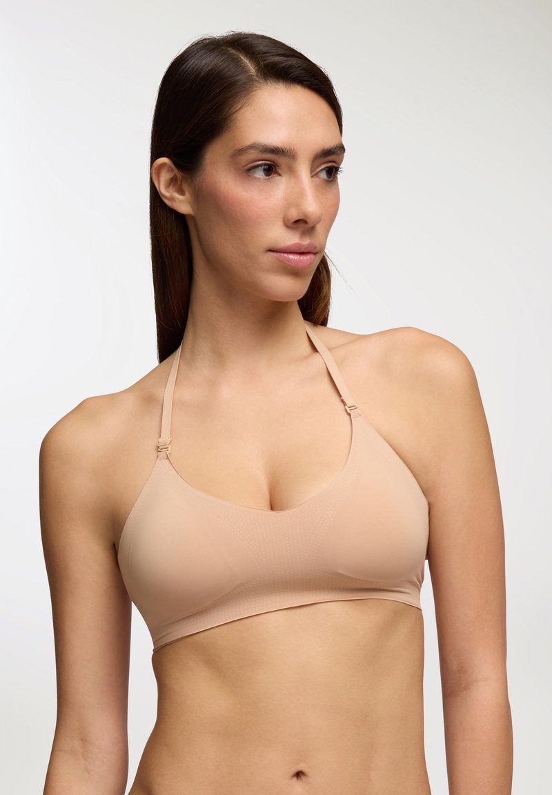 Bralette beige chiaro con una texture liscia e stretchy, design a V, spalline sottili e regolabili, e un delicato motivo a pois sul tessuto.