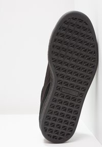 Semelle de basket noire avec un motif de bande de roulement géométrique, présentant un bord lisse et un profil bas. Marquage visible sur la zone de la semelle intermédiaire.