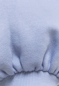 Tissu tricoté bleu clair avec un détail de côte froncée, montrant la texture et l'élasticité en vue rapprochée.