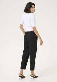 Pantaloni neri su misura con vestibilità dritta, tasche laterali e tasche a filetto posteriori. Abbinati a un top bianco aderente a maniche corte.