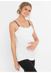 Top premaman bianco con pois neri, dotato di spalline nere regolabili, forma aderente e arricciature sui lati per un maggiore comfort.