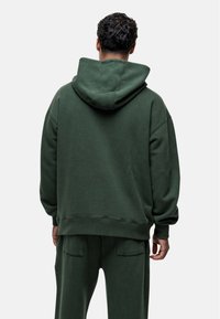 Zielona bluza z kapturem, wykonana z miękkiej, fakturowanej tkaniny. Posiada luźny krój, opadające ramiona oraz kieszeń kangurkę.