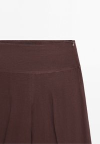 Gonna marrone a vita alta con dettaglio zip laterale e tessuto morbido, mostrata dalla vita a mezza lunghezza.