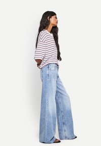 Camicia oversize a righe bianche e rosse abbinata a jeans a gamba larga blu chiaro. Tessuto denim morbido, vestibilità rilassata e caviglie in vista.