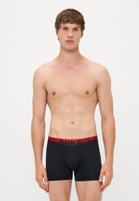 Fekete boxer alsónadrág piros Nike logós derékkal, mely szoros illeszkedésű és sima anyagú. Nincsenek minták vagy díszítések.