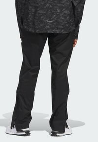Czarne wodoodporne spodnie o prostym kroju nogawek i rozpinanych u dołów, wykonane z lekkiego materiału. Z tyłu znajdują się minimalne elementy z logo.