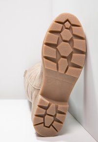 Beżowa podeszwa z zamszu w bucie, z wytrzymałą, teksturowaną gumową spodem o wzorzystym bieżniku zapewniającym przyczepność i stabilność.