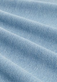 Lyseblåt denimstof med synlig vævningstekstur og bløde folder, der skaber blide bølger på overfladen.