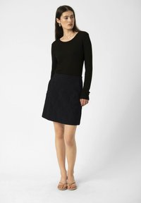 Un haut noir à manches longues associé à une mini-jupe noire texturée. La jupe présente un design simple et une ceinture, complété par des sandales beiges.