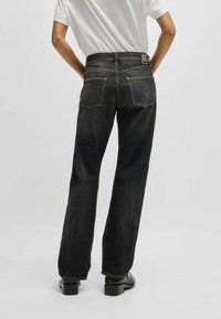 I pantaloni in denim neri presentano un design a gamba dritta con cuciture visibili, due tasche posteriori e un'etichetta in vita. La texture è liscia e resistente.
