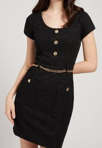 Abito nero realizzato in tessuto testurizzato con scollo rotondo, maniche corte, quattro bottoni dorati e una cintura in catena dorata con due tasche frontali.