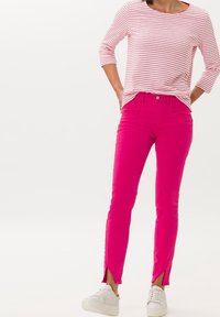 Jeans de mezclilla rosa para mujer con abertura lateral, combinados con una camisa de rayas rojas y blancas de manga larga y zapatillas blancas.