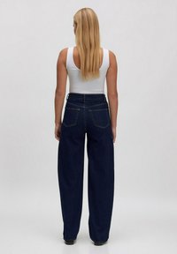 Marineblauwe high-waisted wijde jeans met een textuur van denimafwerking, voorzien van twee achterzakken en een aansluitende tailleband. Witte tanktop zichtbaar.