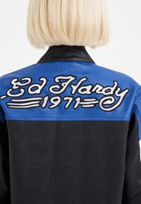 Giacca di pelle nera e blu con ricamo "Ed Hardy 1971" sulla schiena, con una finitura testurizzata e un colletto a contrasto.