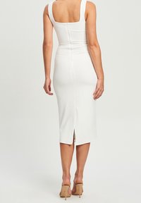 Bílé midi šaty s přiléhavým střihem a čtvercovým výstřihem na zádech, obsahující zip na zadním dílu a rozparek na lemu. Hladká, elastická tkanina. Neutrální vysoké podpatky.