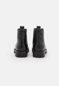 Botas de cuero negras hasta el tobillo con un patrón de cocodrilo, punta redonda, pestañas de tracción y suelas de goma gruesas, que cuentan con una etiqueta de marca en la parte posterior.